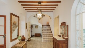 Um corredor com escada, móveis de madeira, um lustre e um espelho grande.