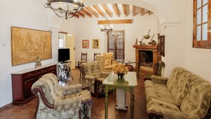 Sala de estar com lareira, vigas de madeira, lustre e móveis antigos.