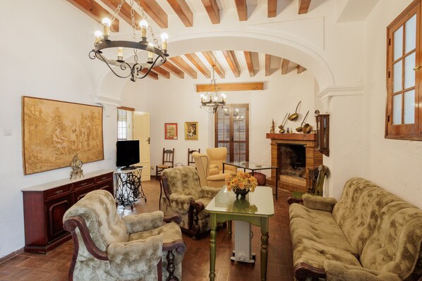 A living room with a fireplace, wooden beams, a chandelier, and antique furniture.
