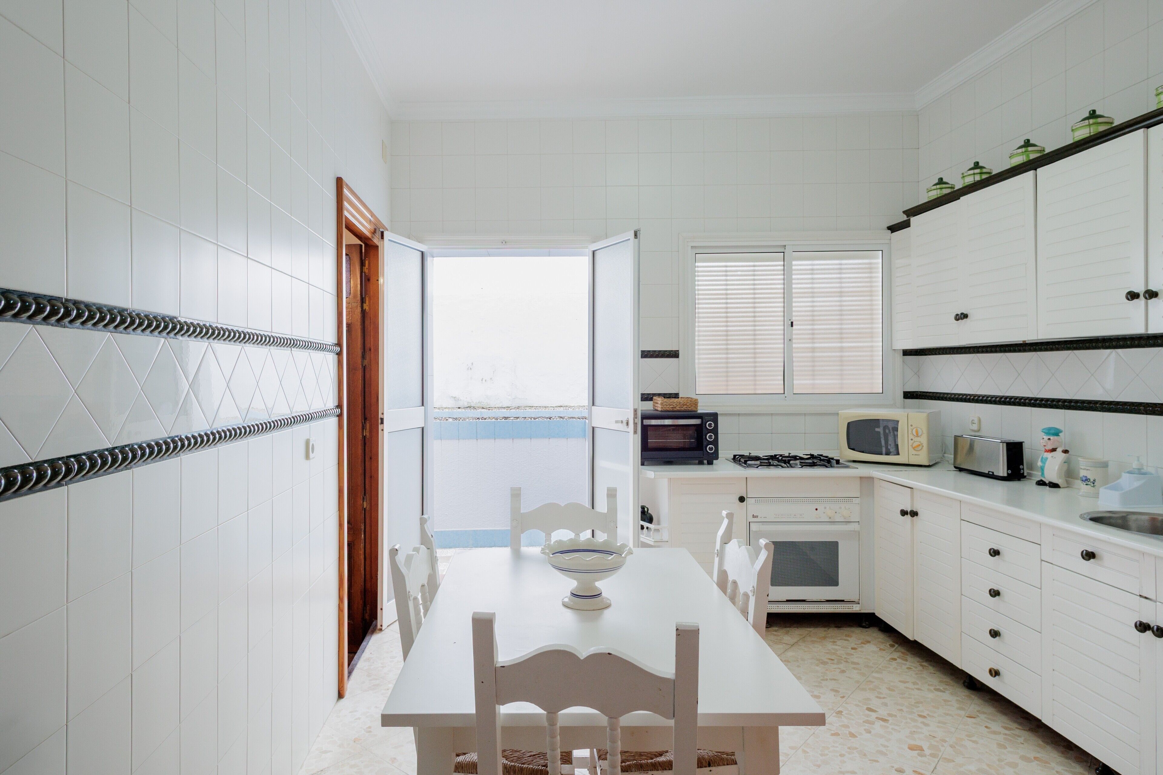 A kitchen with white cabinets, a dining table with chairs, a microwave, a toaster, and a window with blinds.