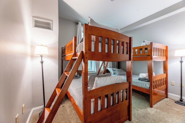 A bunk bed room with a ladder, two bedside lamps, and a window with curtains.