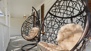 Deux fauteuils à bascule en osier, dotés d’assises rembourrées, se trouvent sur une véranda aux lambris blancs et à la porte en bois.