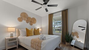 Une chambre à coucher moderne, avec un lit, des tables de chevet, un ventilateur de plafond, une grande fenêtre avec des rideaux et un miroir.