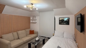 Una habitación de hotel moderna con una cama, un sofá, una mesita de centro y un televisor fijado a la pared.