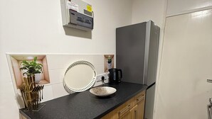 Una cocina con encimera negra, armarios de madera, refrigerador de acero inoxidable, cafetera y planta en maceta.