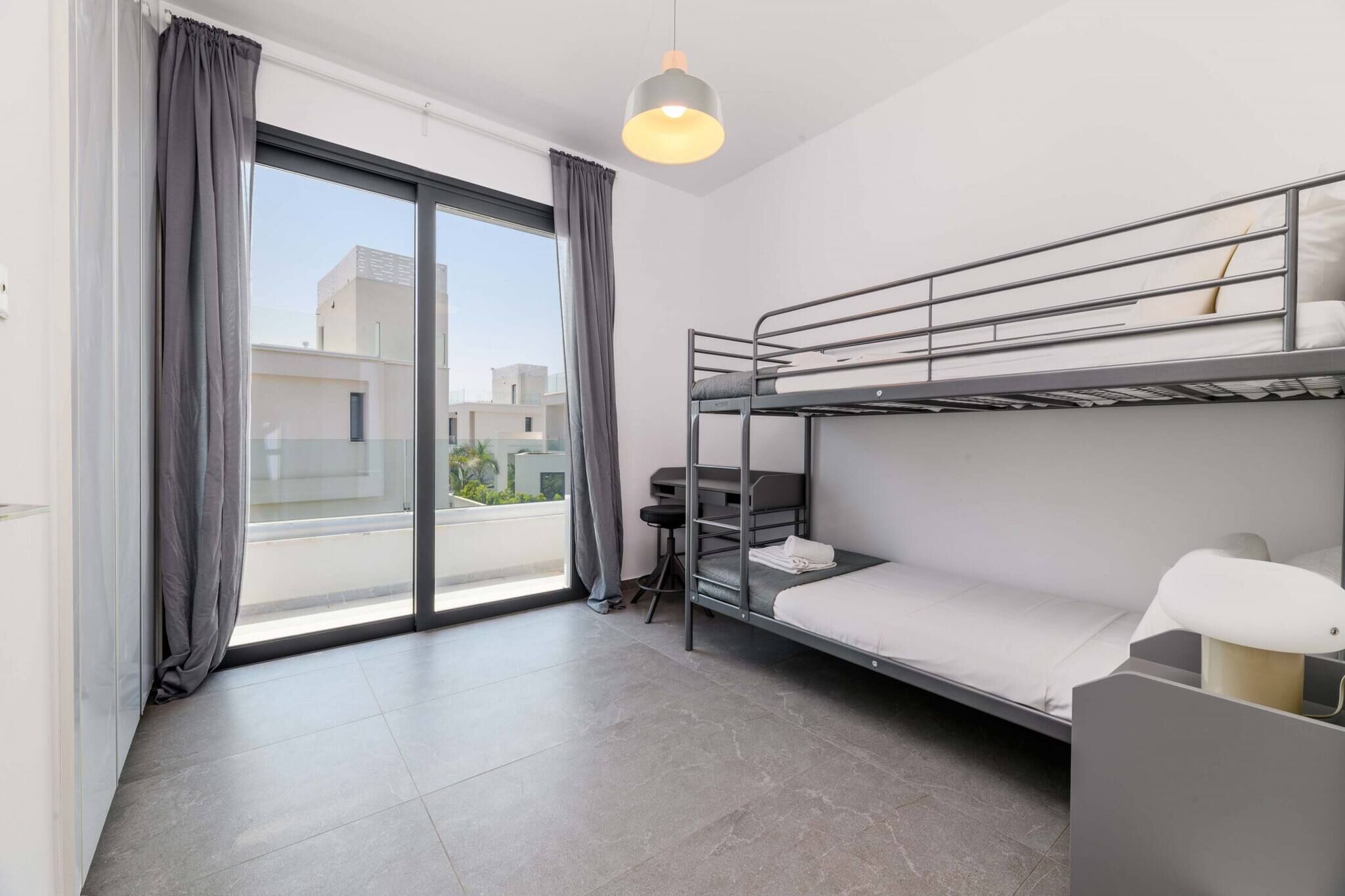 Une chambre d’hôtel moderne avec un lit superposé, un bureau et une grande fenêtre avec des rideaux.