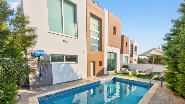 Ein moderner Poolbereich mit rechteckigem Pool, einer integrierten Sitzgelegenheit inklusive Liegestühlen und einem kleinen Garten mit Rasen und Sträuchern.