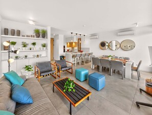 A modern living room with a sofa, coffee table, and chairs, a kitchen area, and a dining space with a table and chairs. - Azure Jade Villa | Luxury Retreat, Private Pool (Protaras)