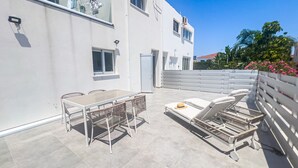 A modern outdoor patio with a dining table and chairs, a sun lounger, and a white fence. - Musan Boutique Studio (Ayia Napa)