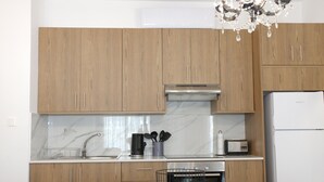 A modern kitchen with wooden cabinets, a stainless steel range hood, a built-in oven, a refrigerator, and a dining area with a table and chairs. - Musan Boutique Inland / Nissi Ave / High-Speed WiFi (Ayia Napa)