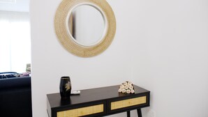 A room with a round woven mirror on the wall, a black console table with wicker drawers, and a vase with flowers on the table. - Musan Boutique Inland / Nissi Ave / High-Speed WiFi (Ayia Napa)