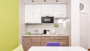 Une cuisine de taille réduite, avec des meubles blancs, un four à micro-ondes, une machine à café et un évier.