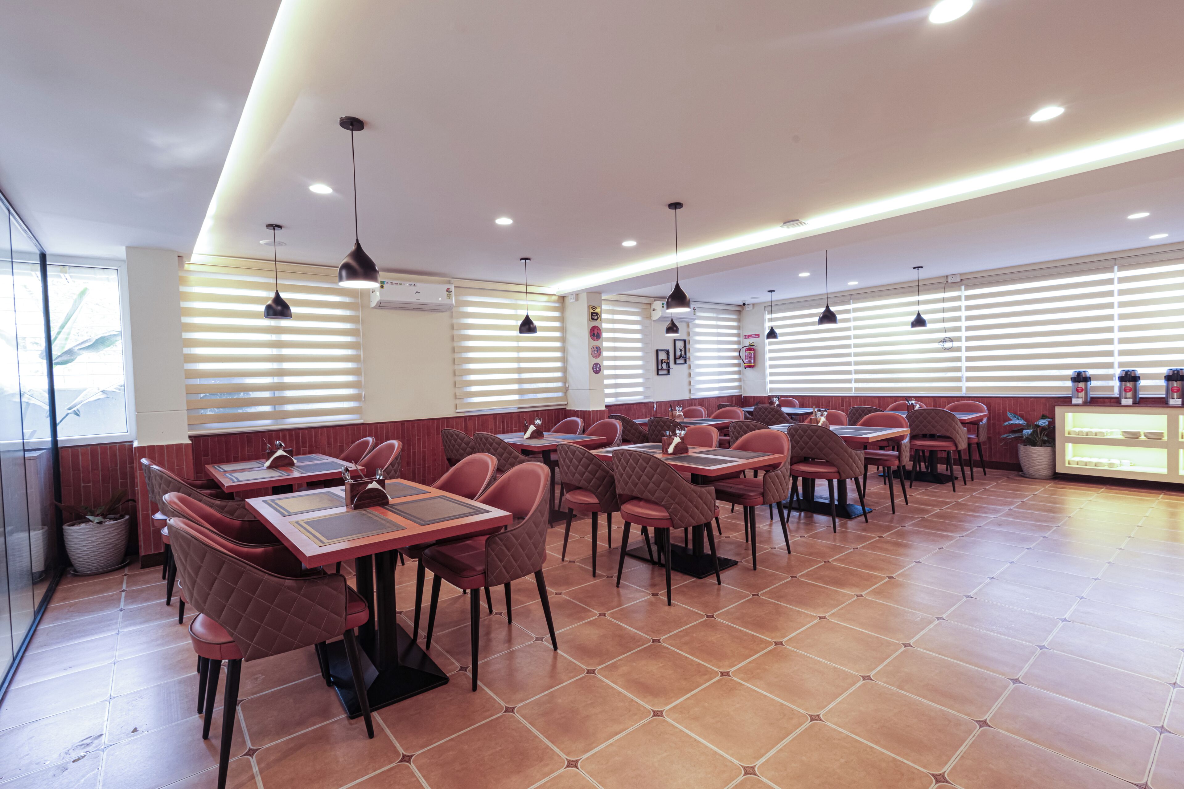 Un restaurant doté de nombreuses tables et chaises, d’un comptoir avec une vitrine réfrigérée et d’un éclairage suspendu.