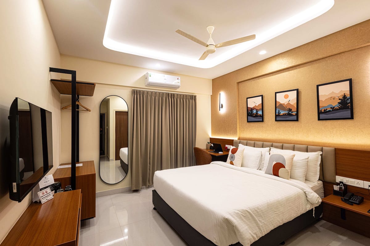 A hotel room with a bed, bedside tables, a desk, a mirror, a ceiling fan, and artwork on the wall.