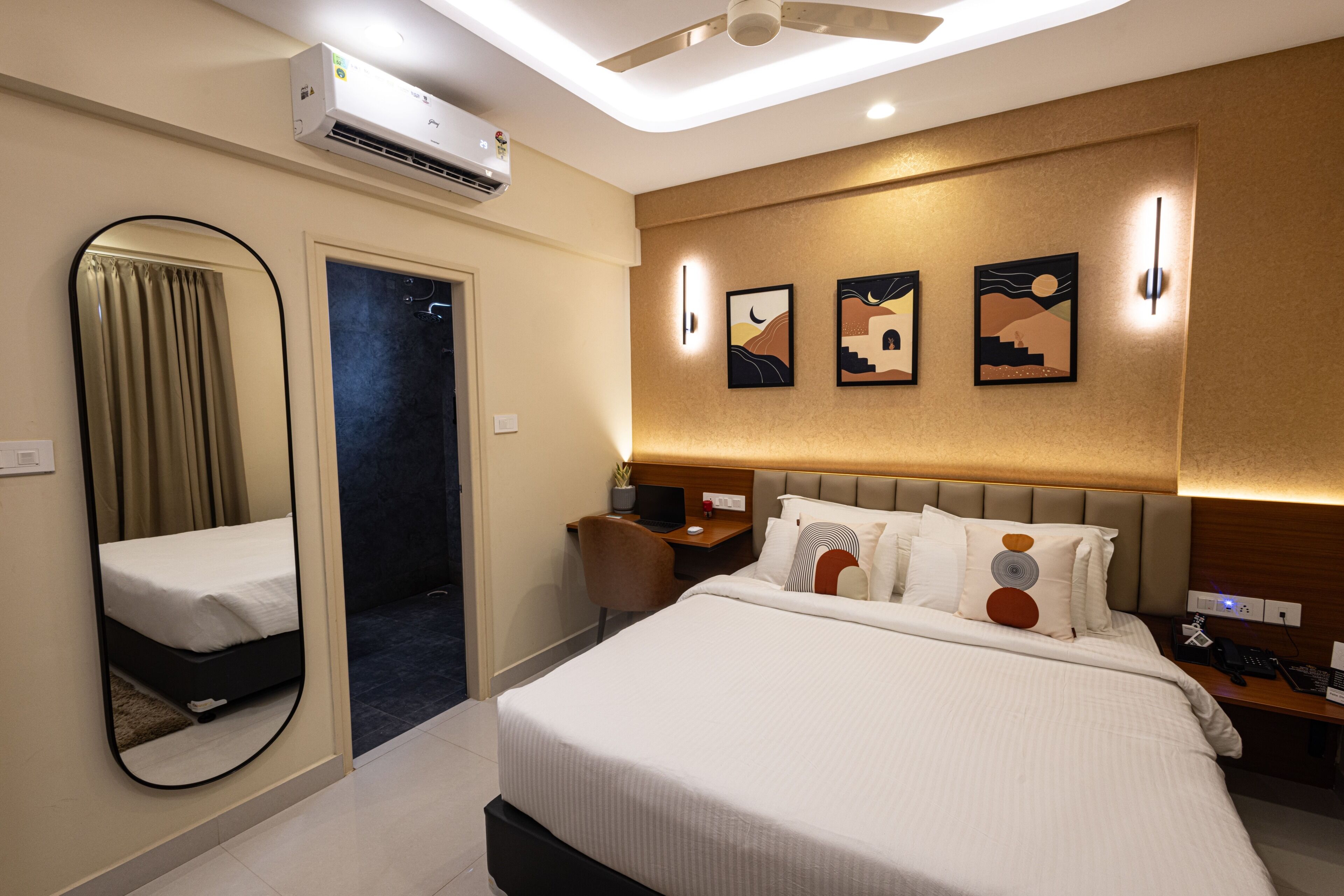 Habitación de hotel con cama, escritorio, silla, espejo y obras de arte en la pared.