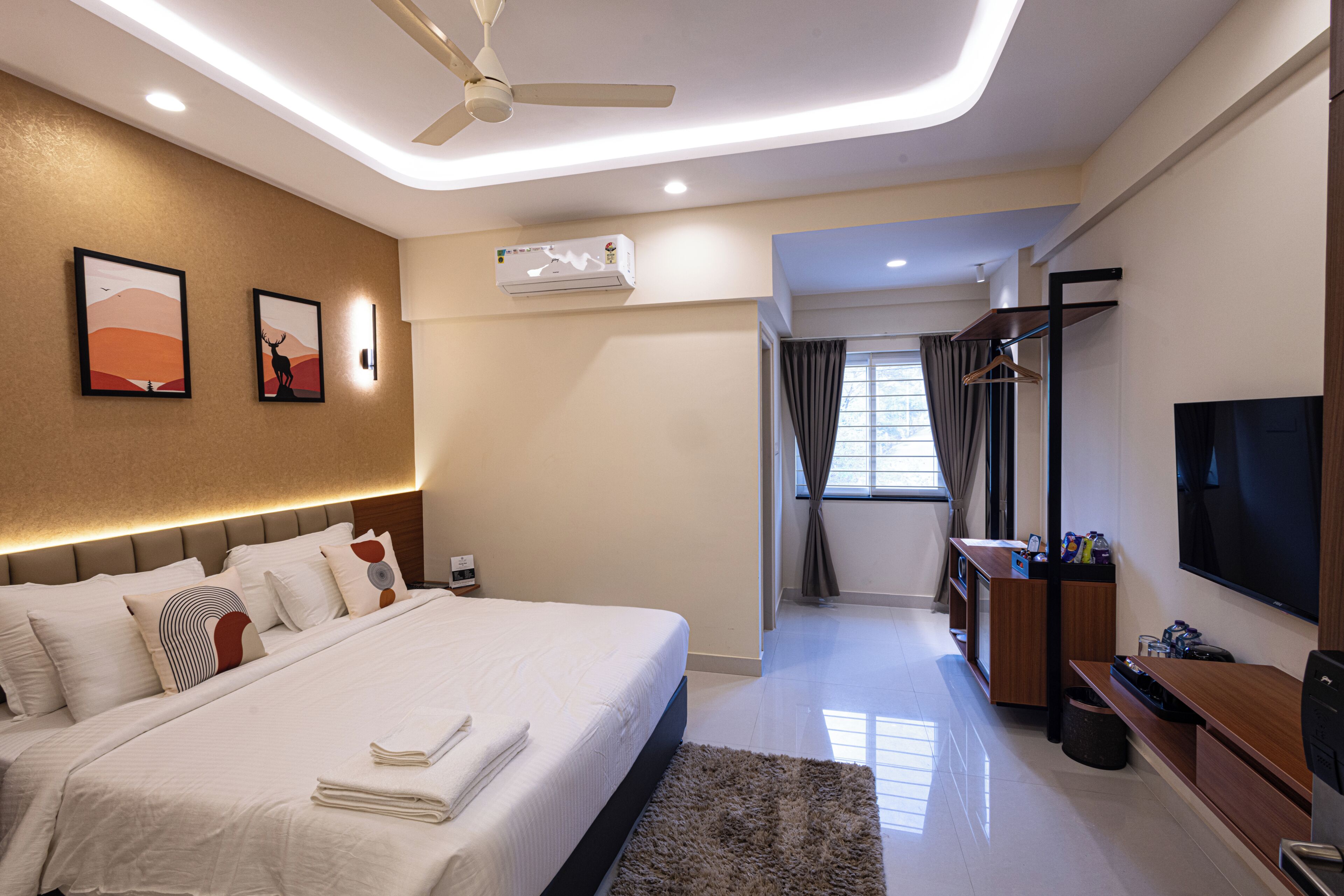 A modern hotel room with a large bed, a TV, a desk, and a ceiling fan.