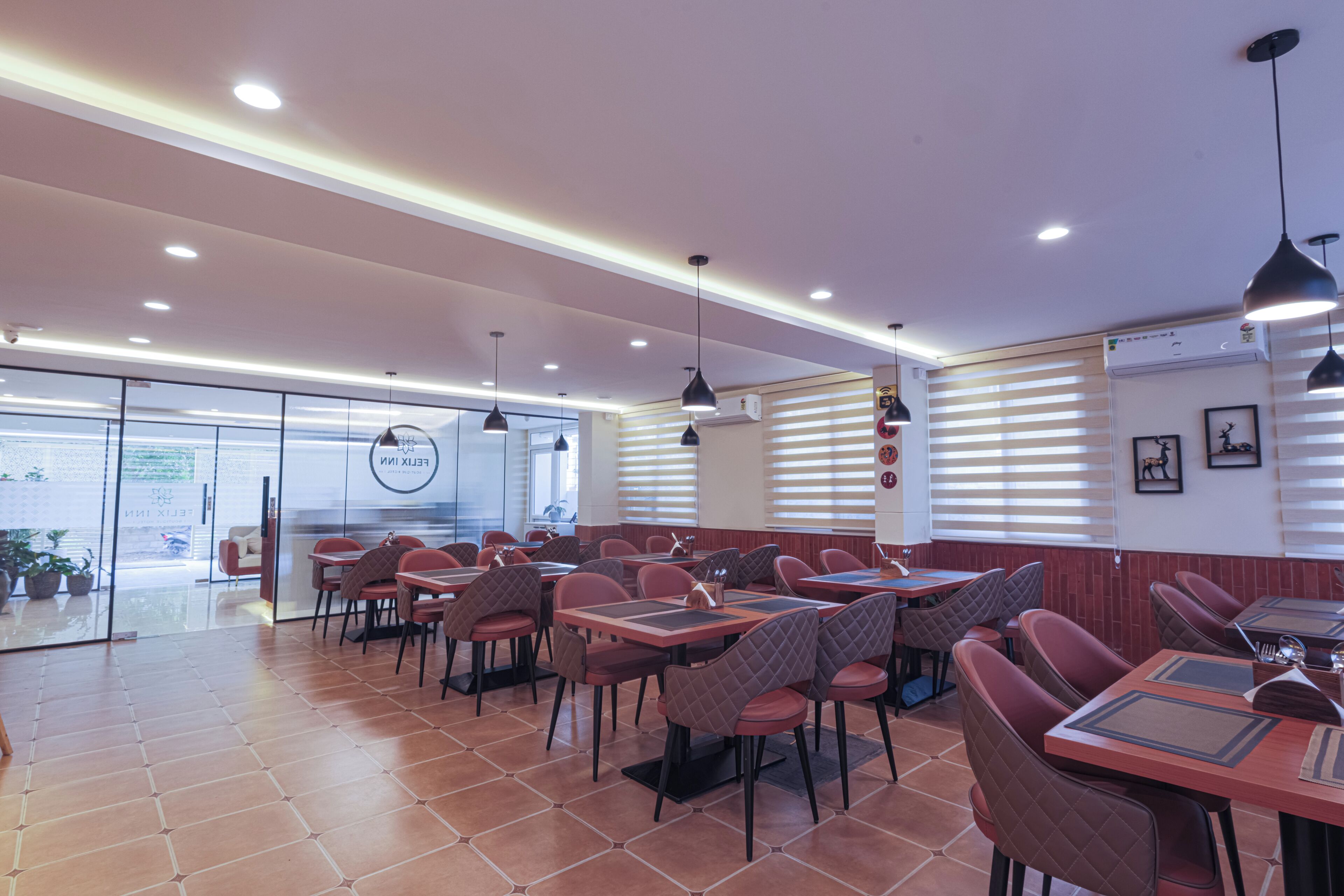 A restaurant interior with tables and chairs, ceiling lights, and a view through the glass wall.