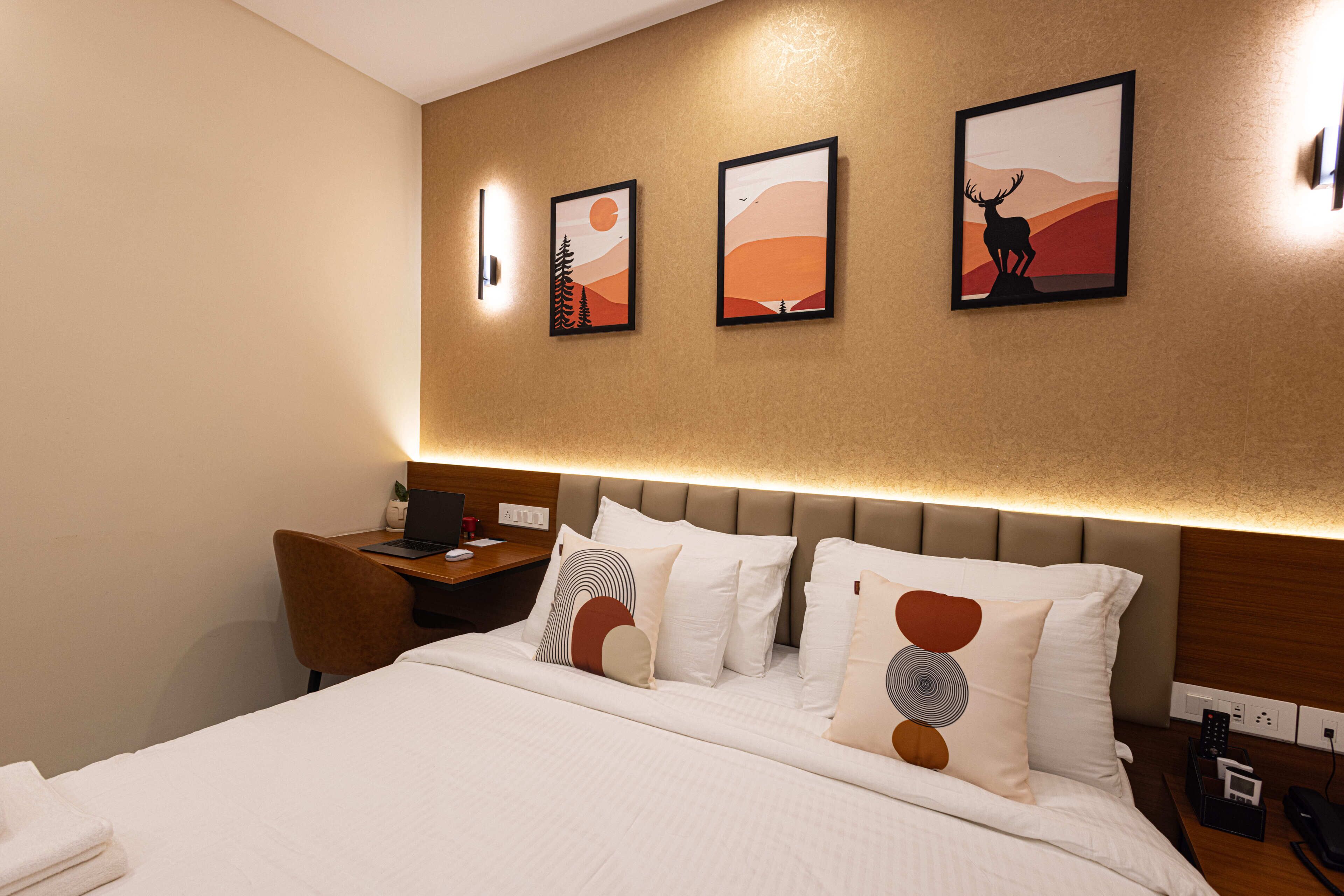 A hotel room with a bed, bedside tables, a desk, and artwork on the wall.