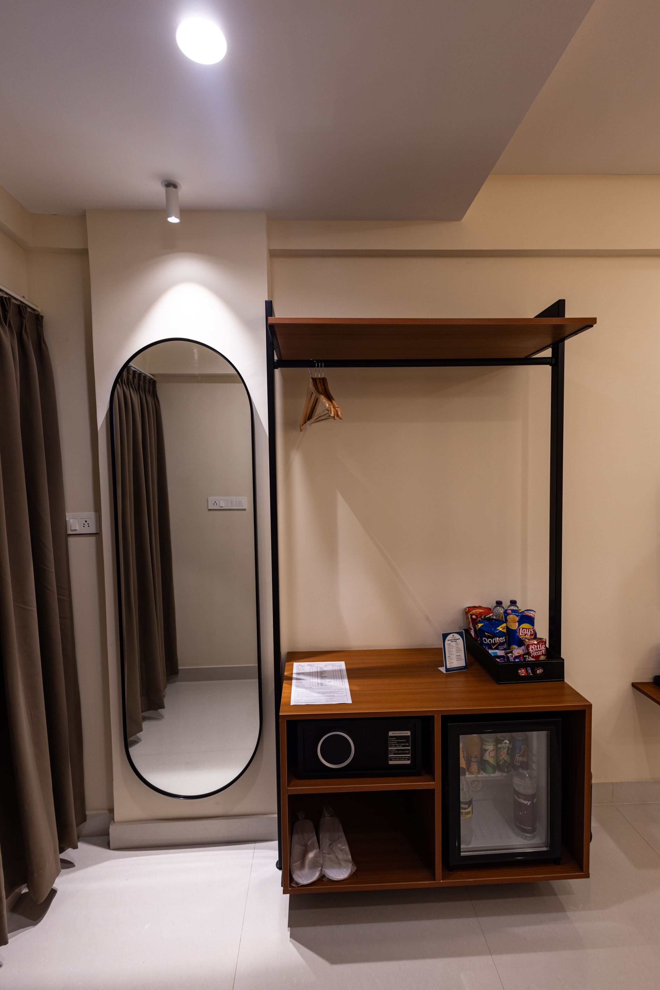 A room with a mirror, a wooden vanity with a mirror, a small refrigerator, and a pair of shoes.