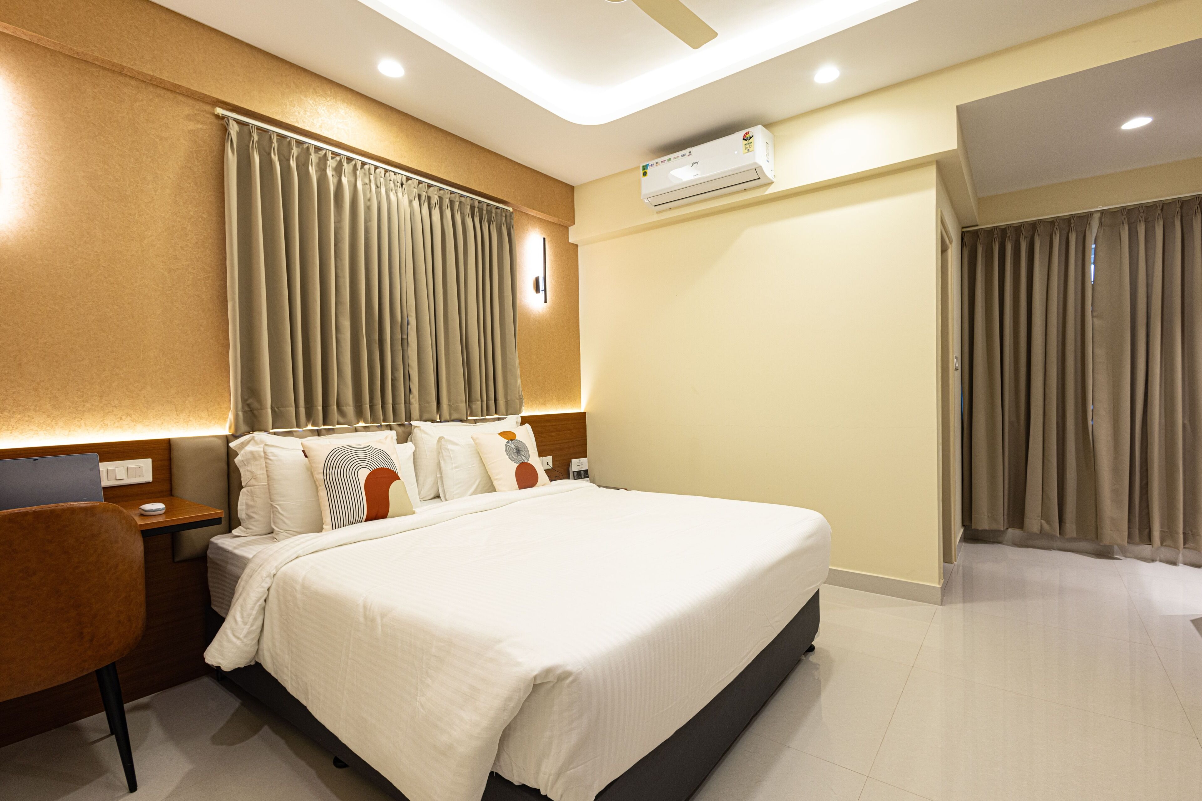 Una habitación de hotel con cama, escritorio, silla, mesita de noche y aire acondicionado.