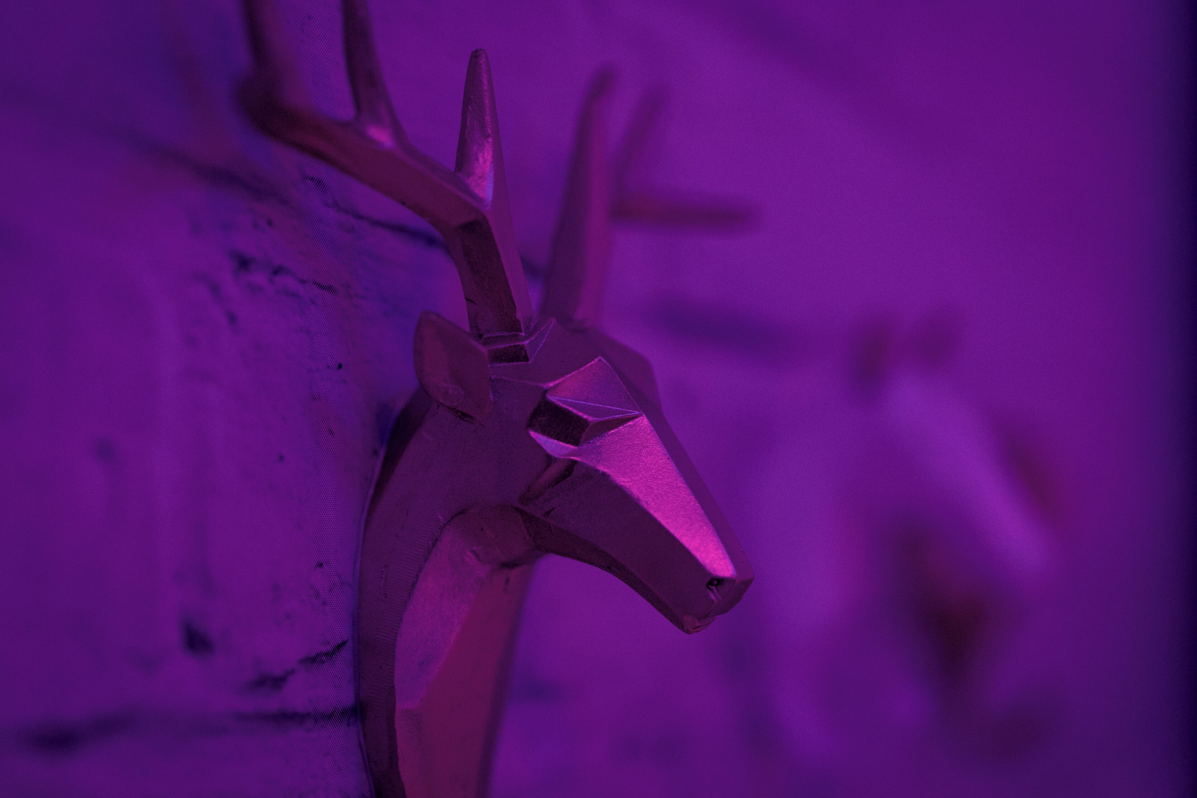 A close-up of a metallic deer head sculpture with a pointed nose and antlers, set against a textured wall.