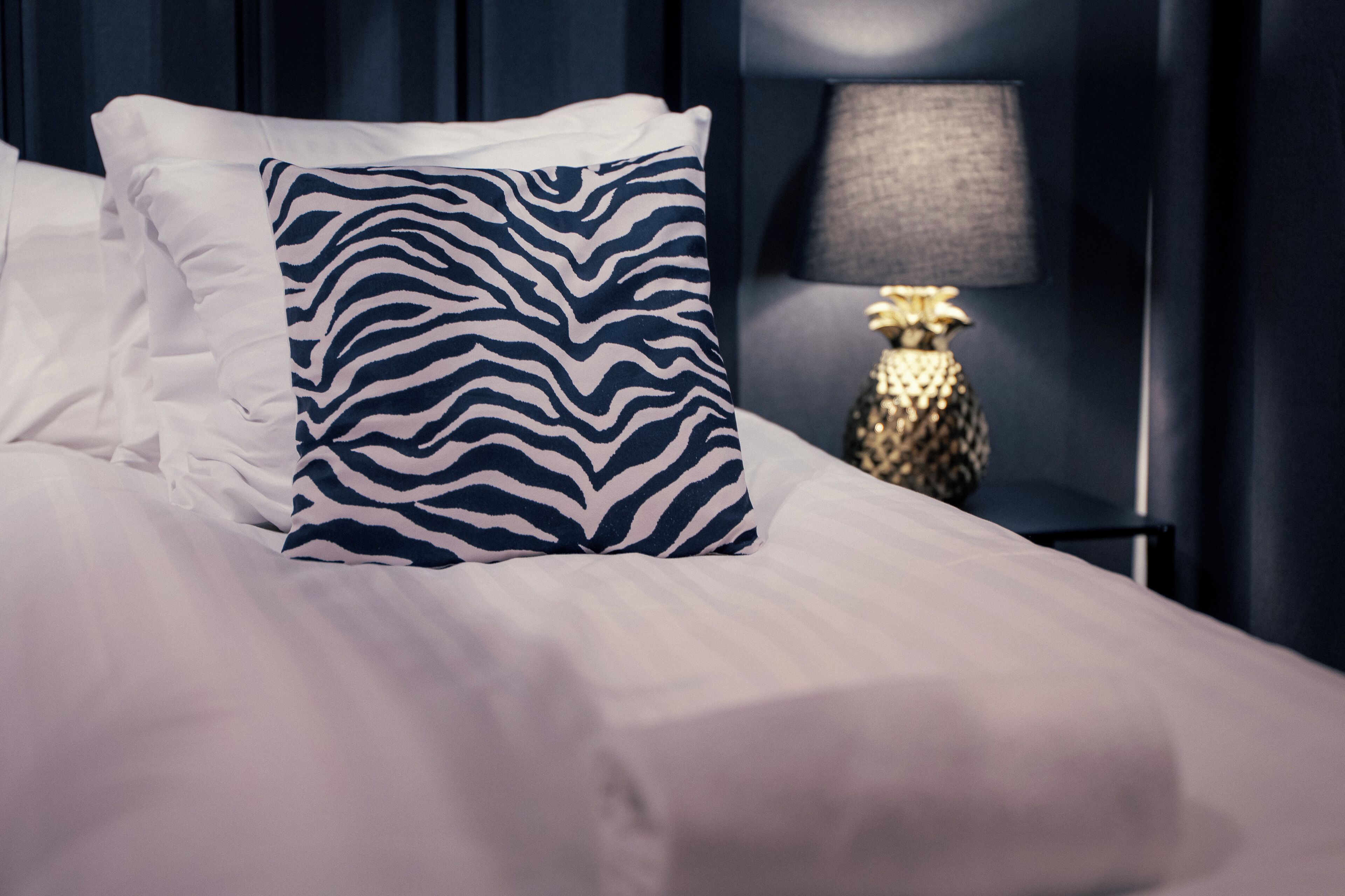 A neatly made bed with white linens and a zebra-patterned pillow.