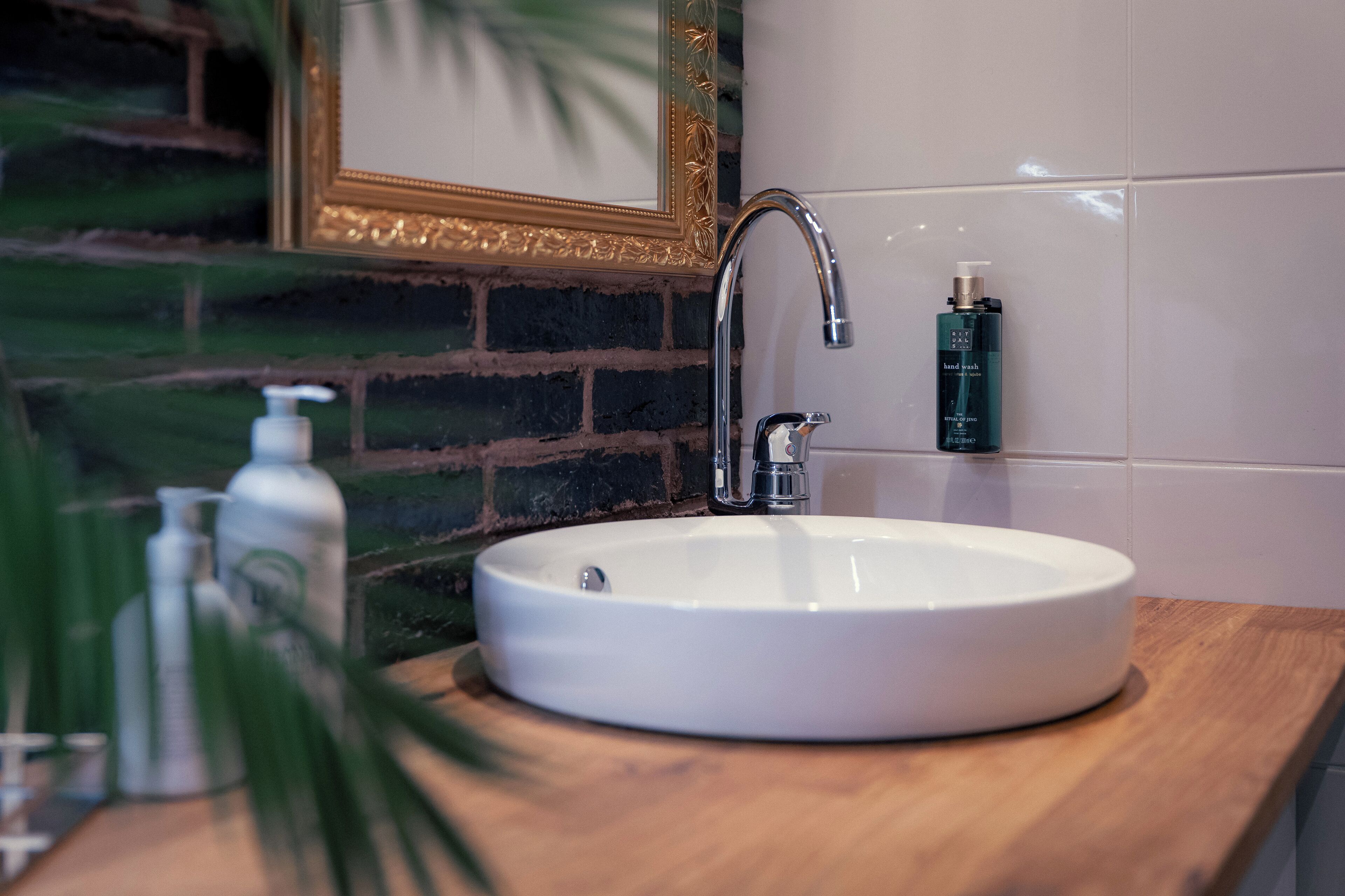 Ein Badezimmer mit einem weißen Waschbecken, einem modernen Wasserhahn und einer Handseifen-Spenderflasche auf der Ablagefläche.