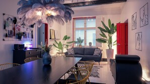 Ein modernes Wohnzimmer mit einem dunklen Holzesstisch, goldenen Stühlen, einem schwarzen Sofa und einer roten Tür.