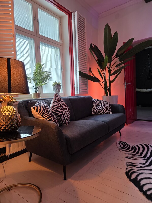 A living room with a dark grey sofa, zebra-patterned cushions, a glass coffee table with a pineapple centerpiece, a large potted plant, and a zebra-patterned rug. - XoXo Apartments Tampere City (Tampere)
