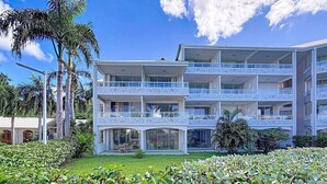 A multi-story hotel with balconies, surrounded by lush greenery and palm trees. - La Case à Sucre – Peaceful retreat, sea view, beach front (Anse Marcel)