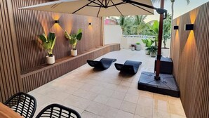 Un espace patio extérieur agrémenté d’un mur en bois, de plantes en pot, d’un grand parasol et de mobilier moderne.