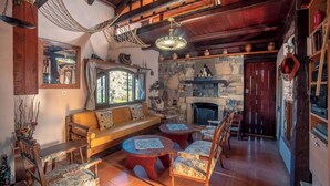 Un interior acogedor y rústico con chimenea de piedra, vigas de madera y un espacio de estar cómodo con sofá y sillones.