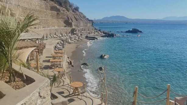 Una playa costera con asientos de piedra y un acantilado rocoso.
