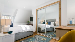 A modern bedroom with a large mirror, a bed with white linens, a bedside table with a lamp, and a wooden desk with a glass container. - Rutherglen - sleeps 4 guests  in 2 bedrooms (Beaumaris)