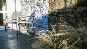 A patio with outdoor seating, a stone wall, and tall grasses. - Rutherglen - sleeps 4 guests  in 2 bedrooms (Beaumaris)