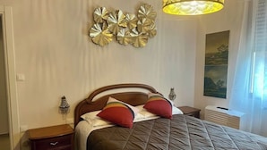 A neatly made bed with a brown quilt, two red pillows, and a wooden headboard. There is a wall-mounted decorative piece above the bed and a painting on the wall to the right. - Il Torrione - Cozy Independent House for 4, between History and Relaxation (Castel Bolognese)