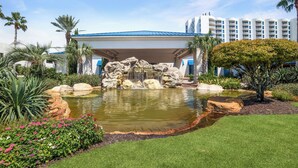 A hotel with a covered outdoor area featuring a rock waterfall, a pond, and a well-maintained garden with various plants and flowers. - The Palms Destin 2103 (Destin)
