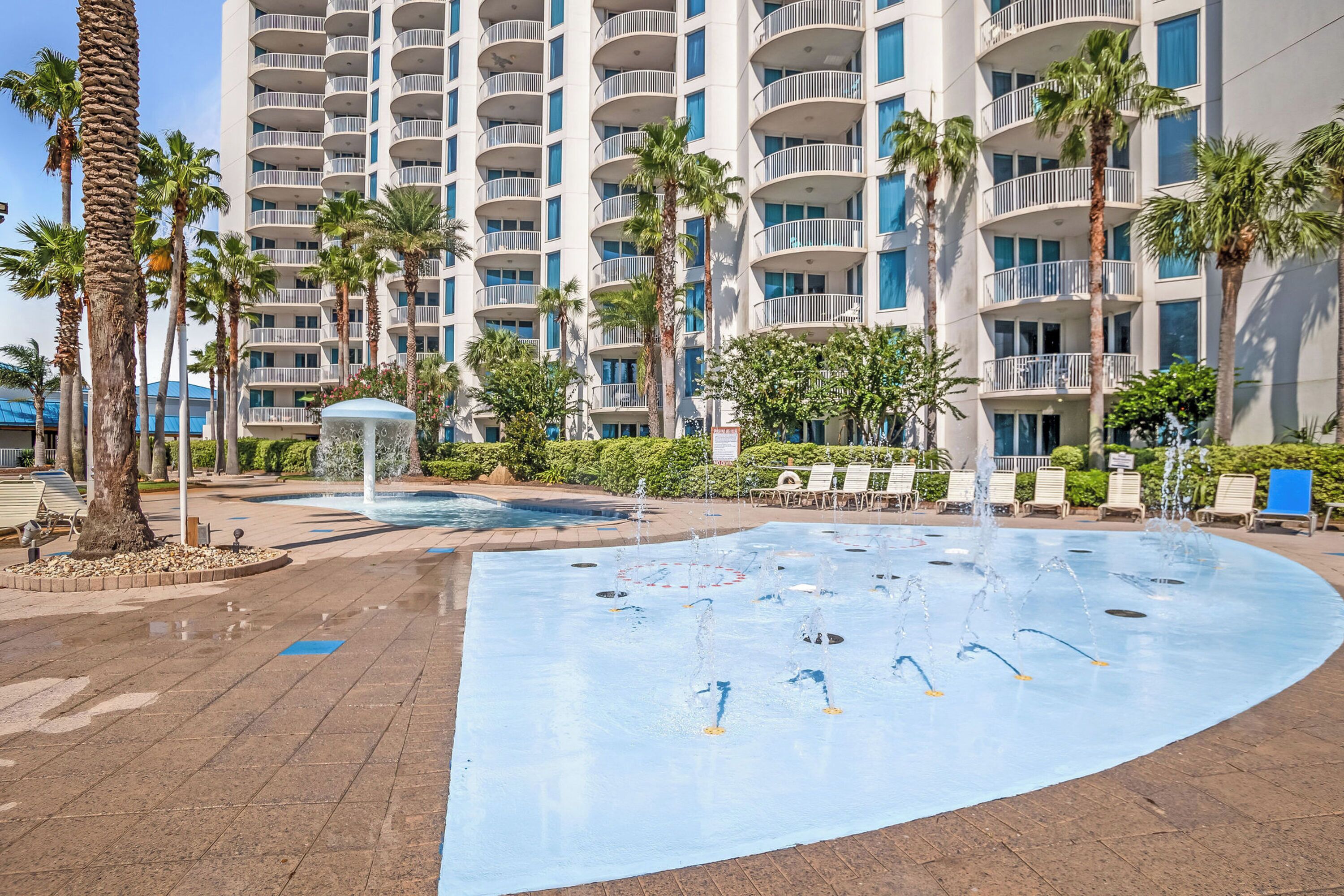 Un espace piscine d’hôtel avec une grande piscine, des palmiers et un immeuble à plusieurs étages en arrière-plan.