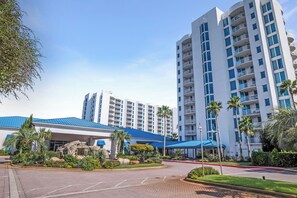 A modern hotel with a blue-roofed entrance, a parking area, and a well-maintained garden. - The Palms Destin 2103 (Destin)