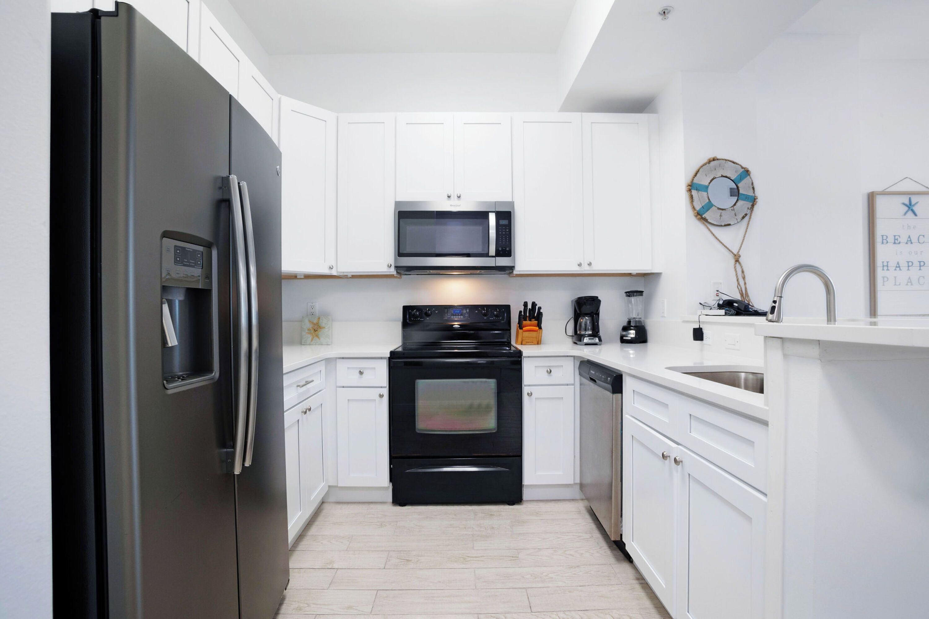 A modern kitchen with white cabinetry, a stainless steel refrigerator, a microwave, an oven, and a dishwasher.