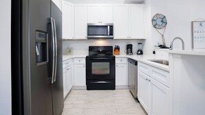 A modern kitchen with white cabinetry, a stainless steel refrigerator, a microwave, an oven, and a dishwasher. - The Palms Destin 2103 (Destin)