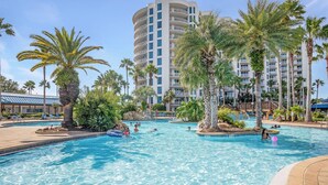 A swimming pool with clear blue water, surrounded by palm trees and a multi-story building with balconies. - The Palms Destin 2103 (Destin)