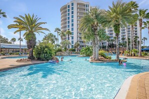 A swimming pool with clear blue water, surrounded by palm trees and a multi-story building with balconies. - The Palms Destin 2103 (Destin)