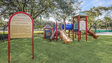 Un parque infantil con un tobogán, estructuras para escalar y una zona vallada.