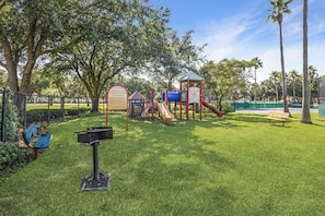 A playground with slides and climbing structures, surrounded by grass and trees. - The Palms Destin 2103 (Destin)