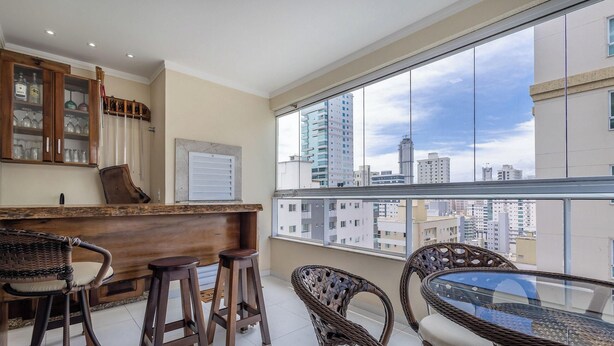 A balcony with wicker furniture, a bar area with stools, and a view of the cityscape. - Apt w/ BBQ & Balcony, 450m From the Beach Sit1202 (Itapema)