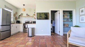 Cocina compacta con electrodomésticos modernos, un área de comedor con sofá blanco y un pasillo que lleva a un baño.
