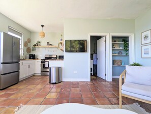 Eine kompakte Küche mit modernen Geräten, ein Essbereich mit einem weißen Sofa und ein Flur, der zum Badezimmer führt.
