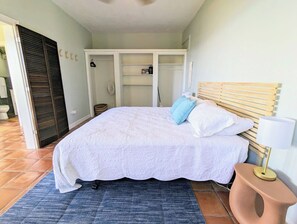 Ein Schlafzimmer mit Bett, Nachttisch, Kleiderschrank und einem durchgegangenen Tür sichtbaren Badezimmer.
