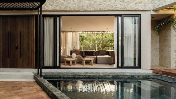 Un área exterior moderna con piscina, terraza de madera y zona de estar con sofá y mesa de centro.